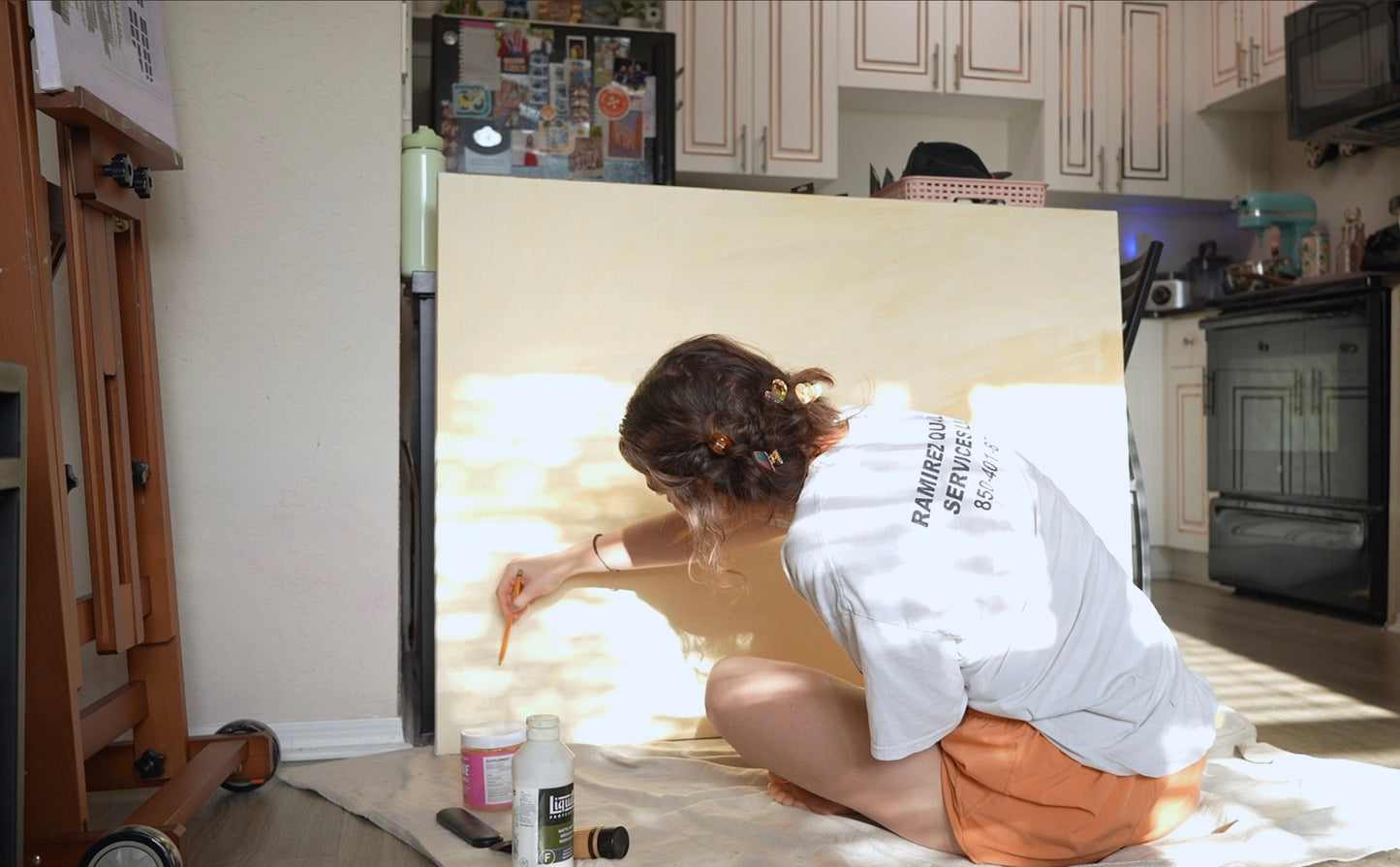Person sitting on the floor in a kitchen with a large white Canvas leaning against the wall.