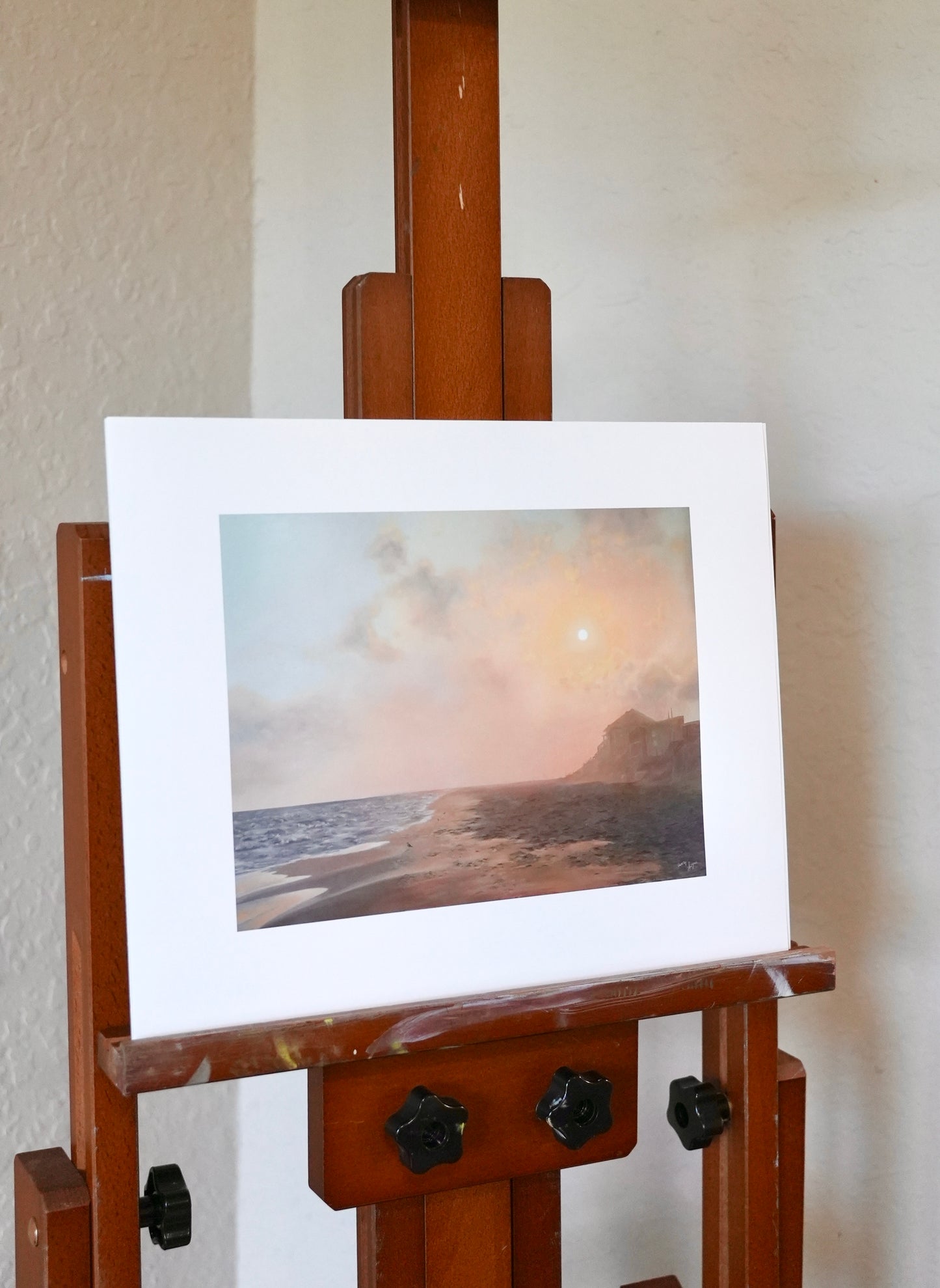 Wooden easel with an art print of a landscape on a white wall.