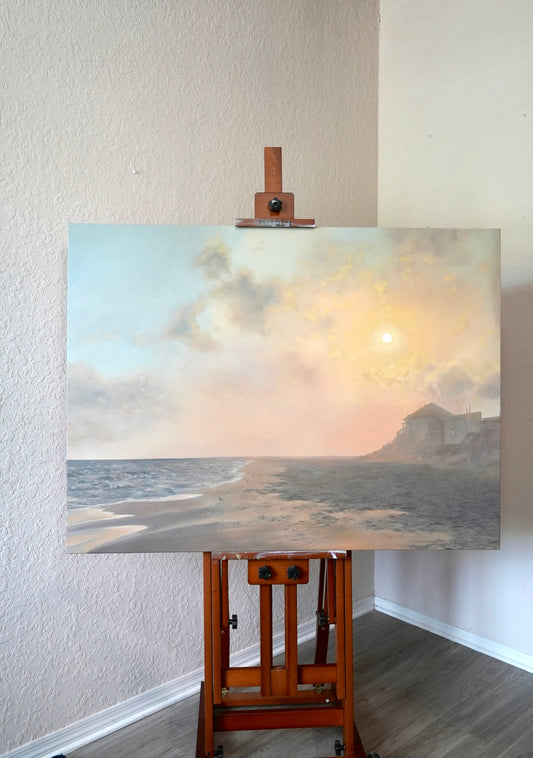 Painting of a coastal scene on an easel against a white wall.