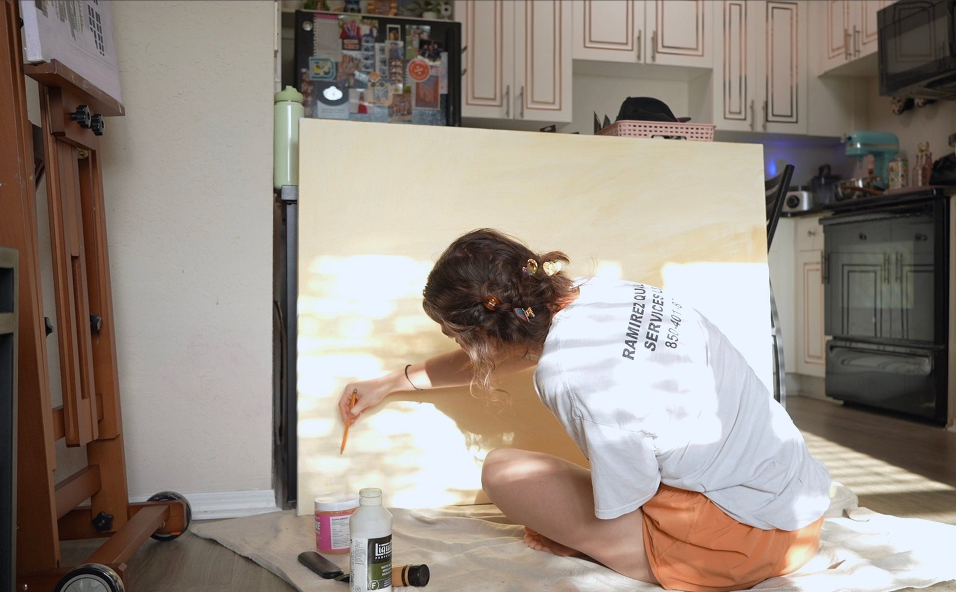 Person sitting on the floor in a kitchen with a large white Canvas leaning against the wall.
