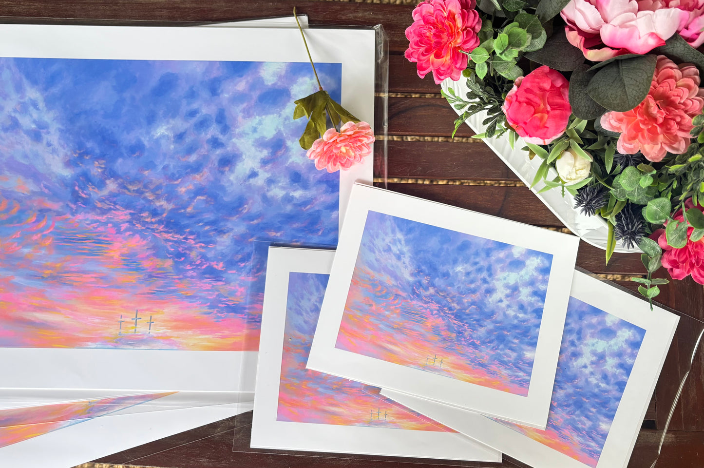 Prints of a colorful sky with pink and green flowers on a wooden surface