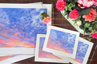 Prints of a colorful sky with pink and green flowers on a wooden surface