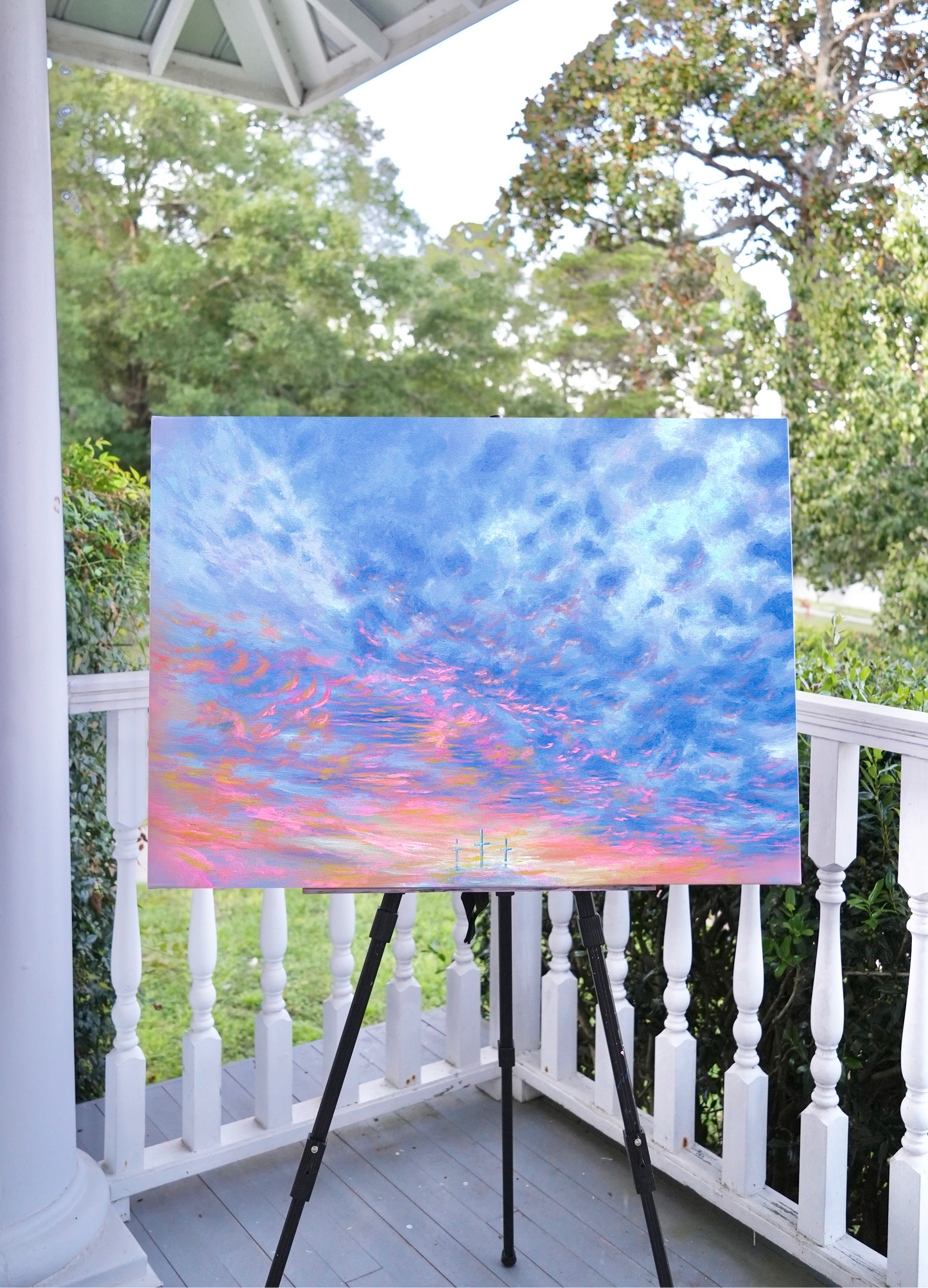 Painting of a colorful sky on an easel outdoors with trees in the background