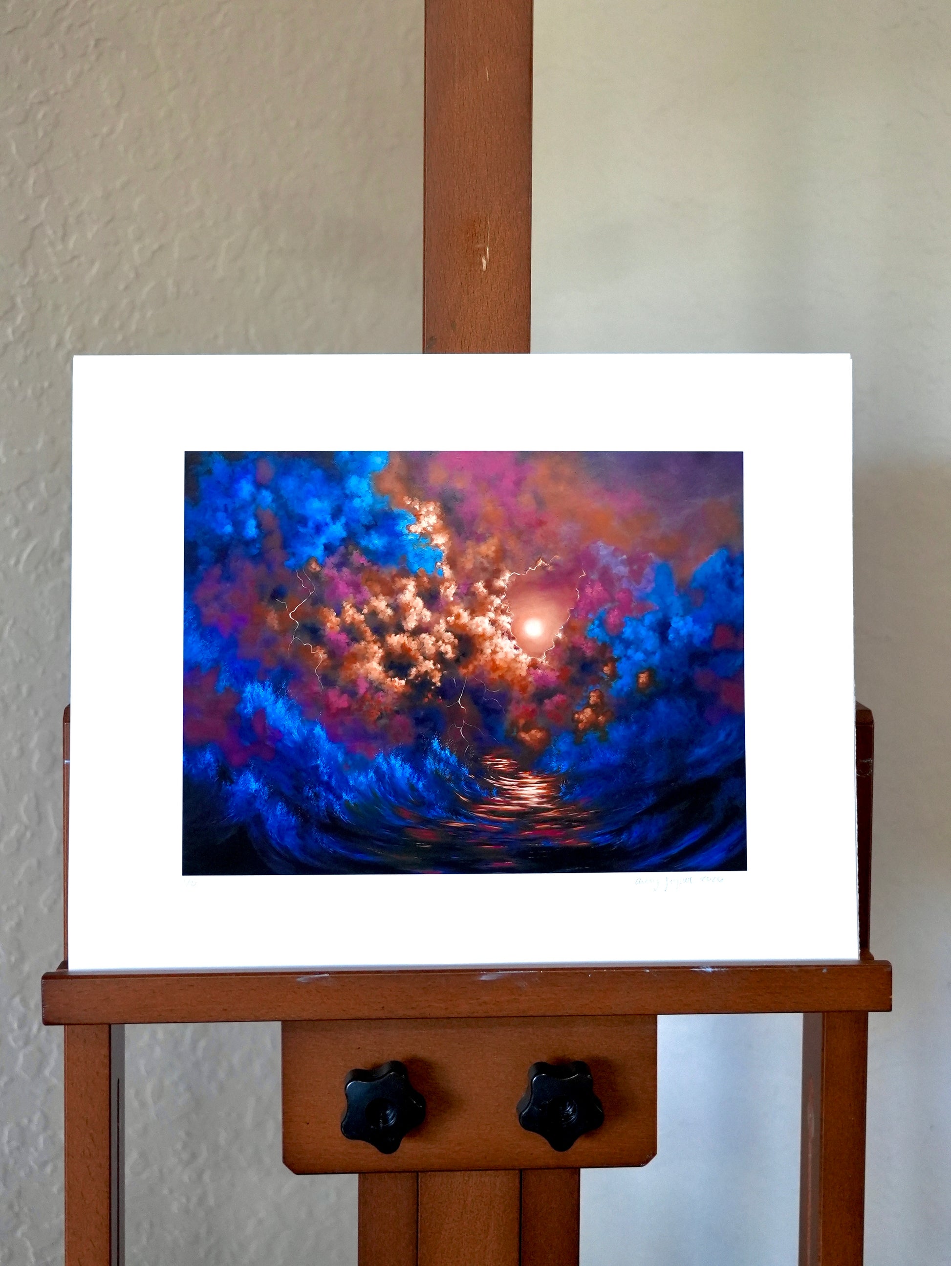 Abstract artwork on a white mat displayed on a wooden easel against a plain wall.