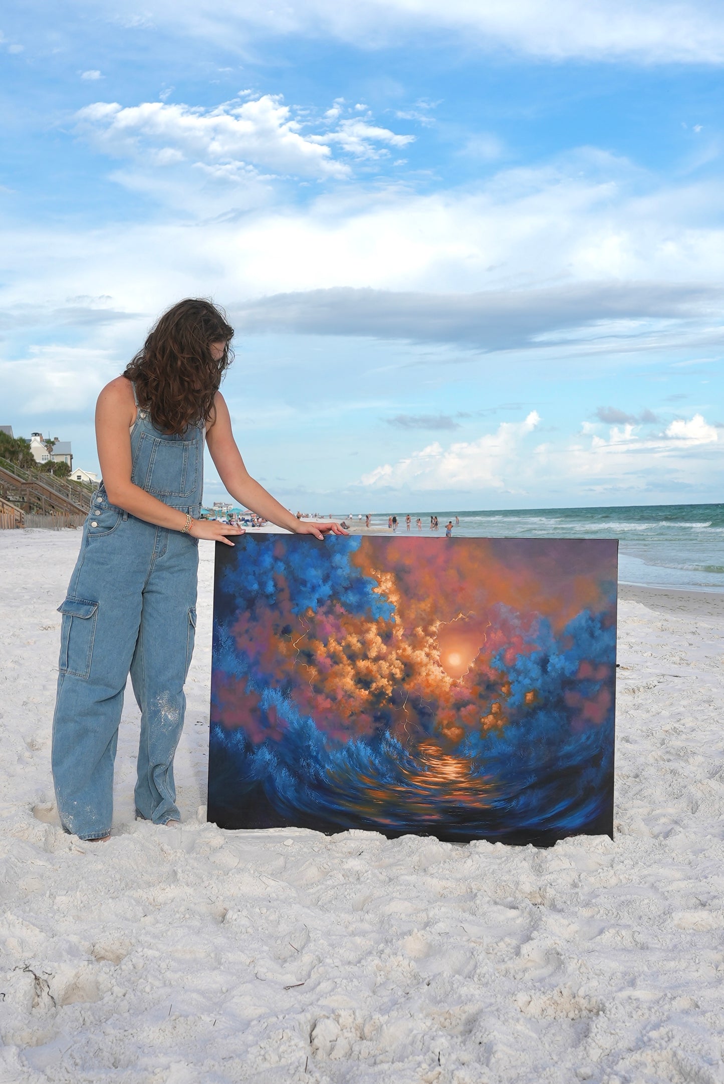 Avery holding a large abstract painting on a beach with ocean and sky in the background