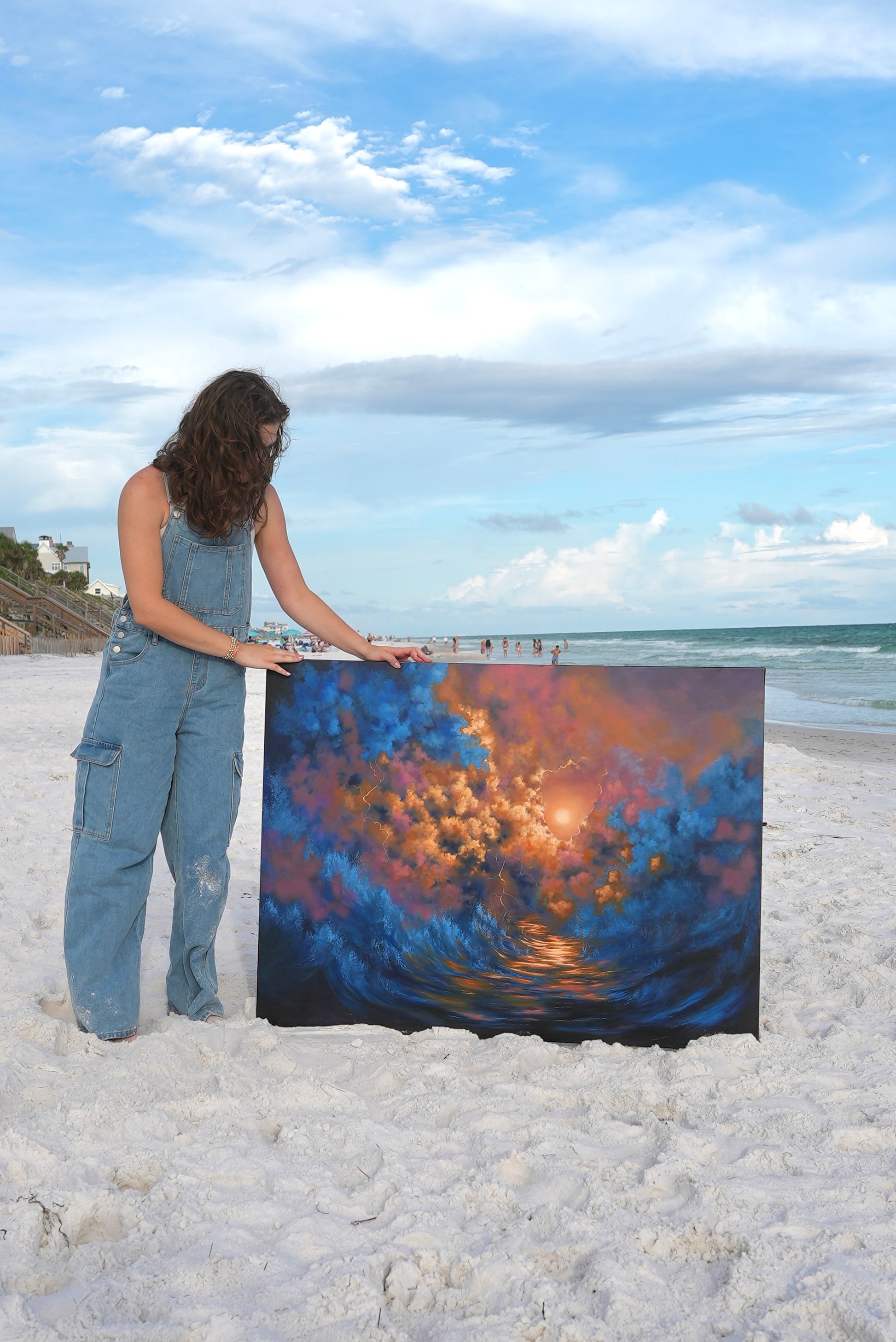 Avery holding a large abstract painting on a beach with ocean and sky in the background