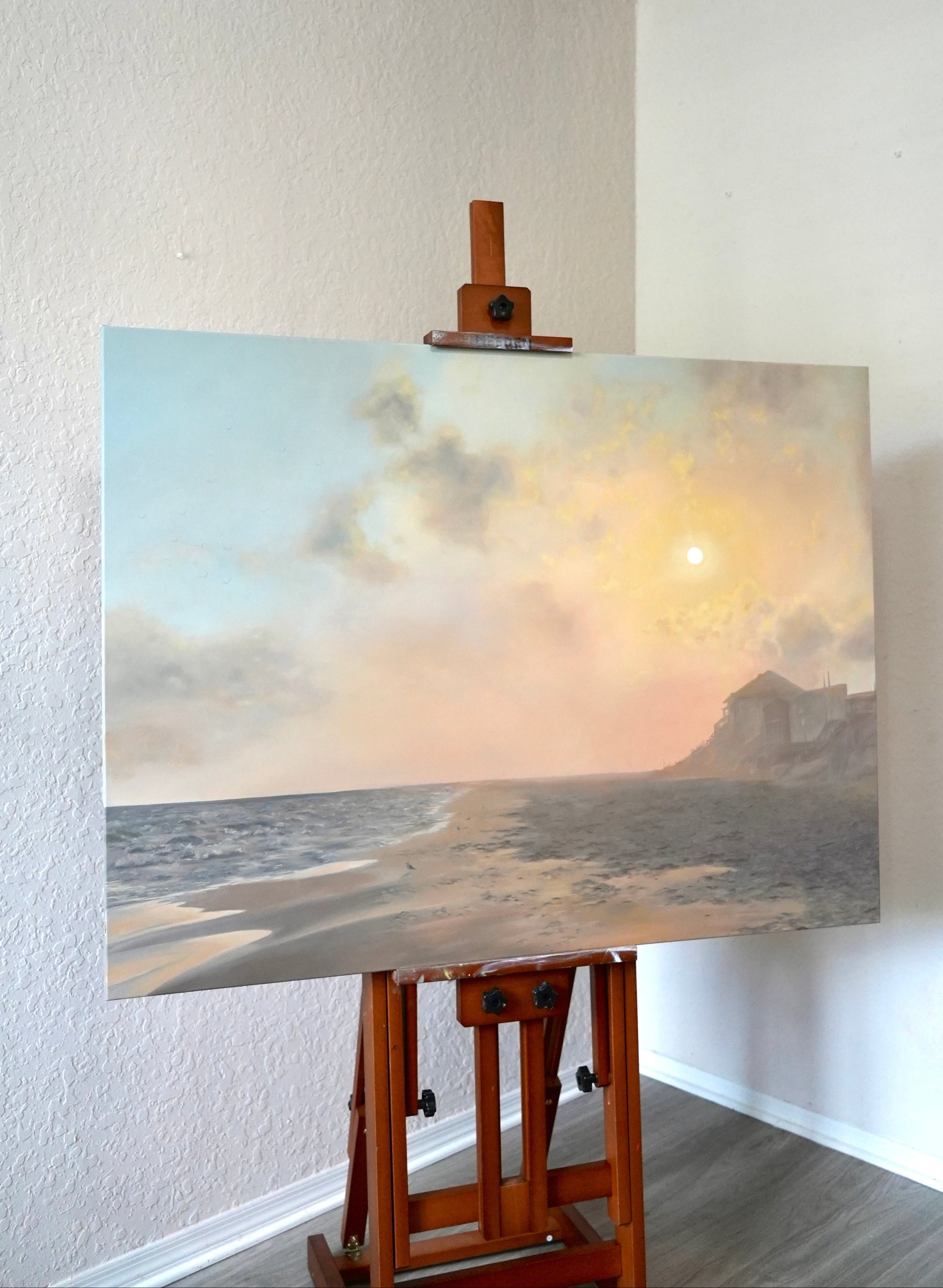 Painting of a coastal scene on an easel against a white wall