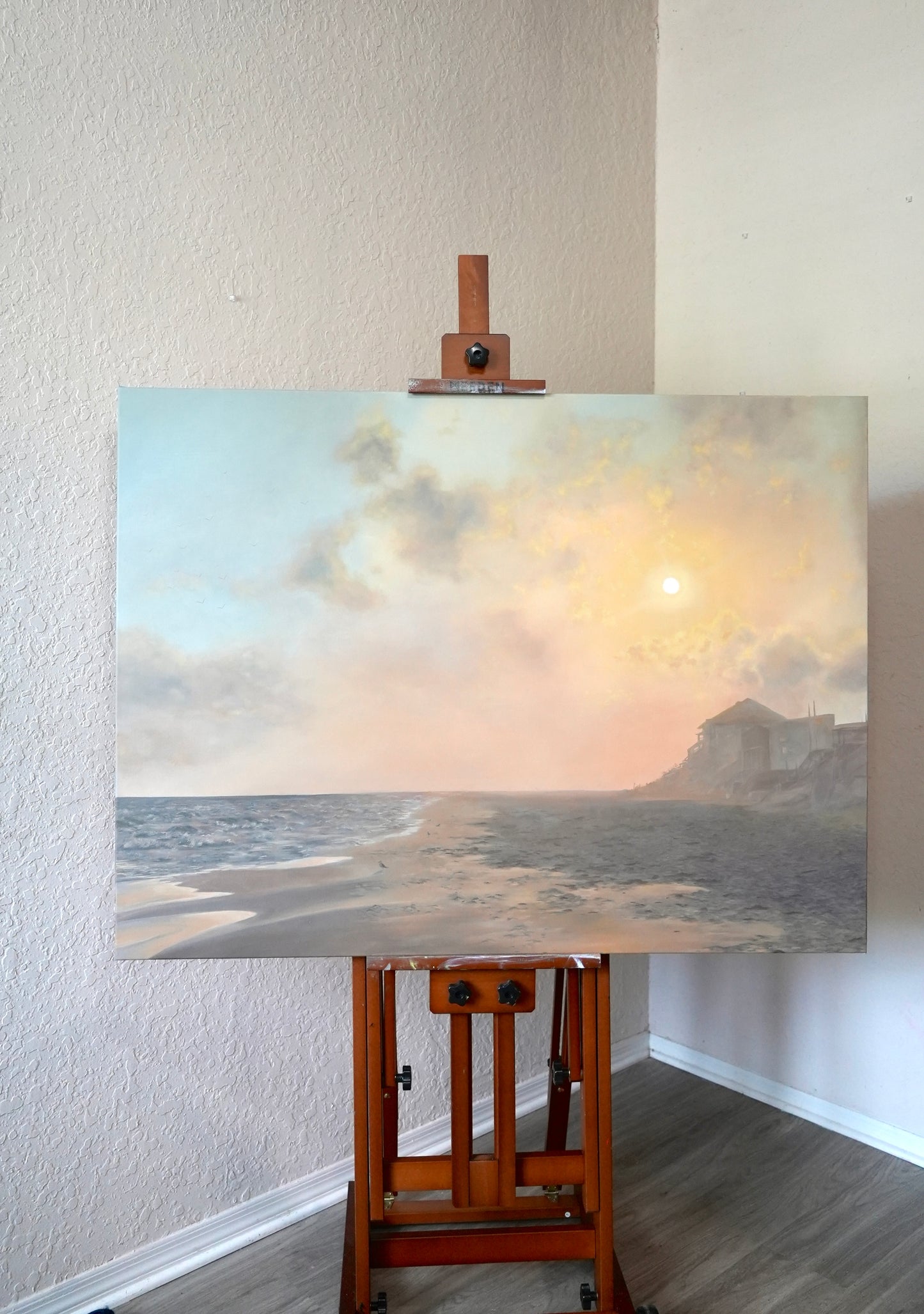 Painting of a coastal scene on an easel against a white wall.