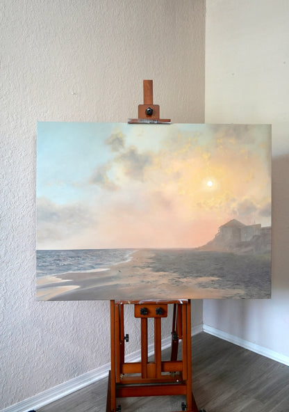 Painting of a coastal scene on an easel against a white wall.