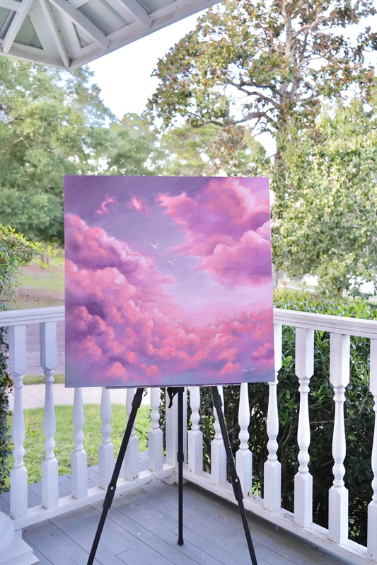 Painting of pink and purple clouds on an easel outdoors.