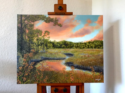 Painting of a landscape with trees, sky, and water on an easel.