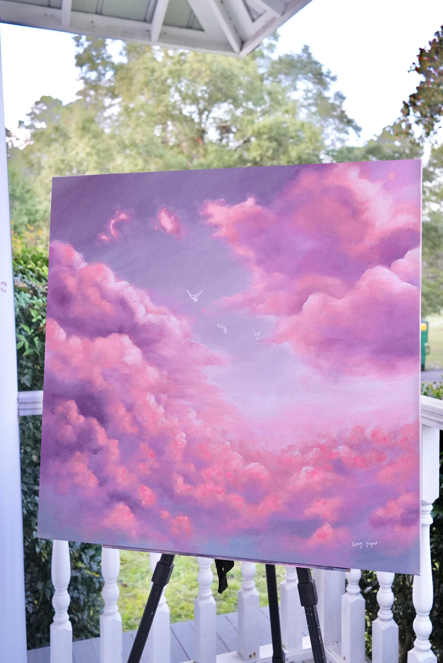Painting of pink and purple clouds on an easel outdoors.